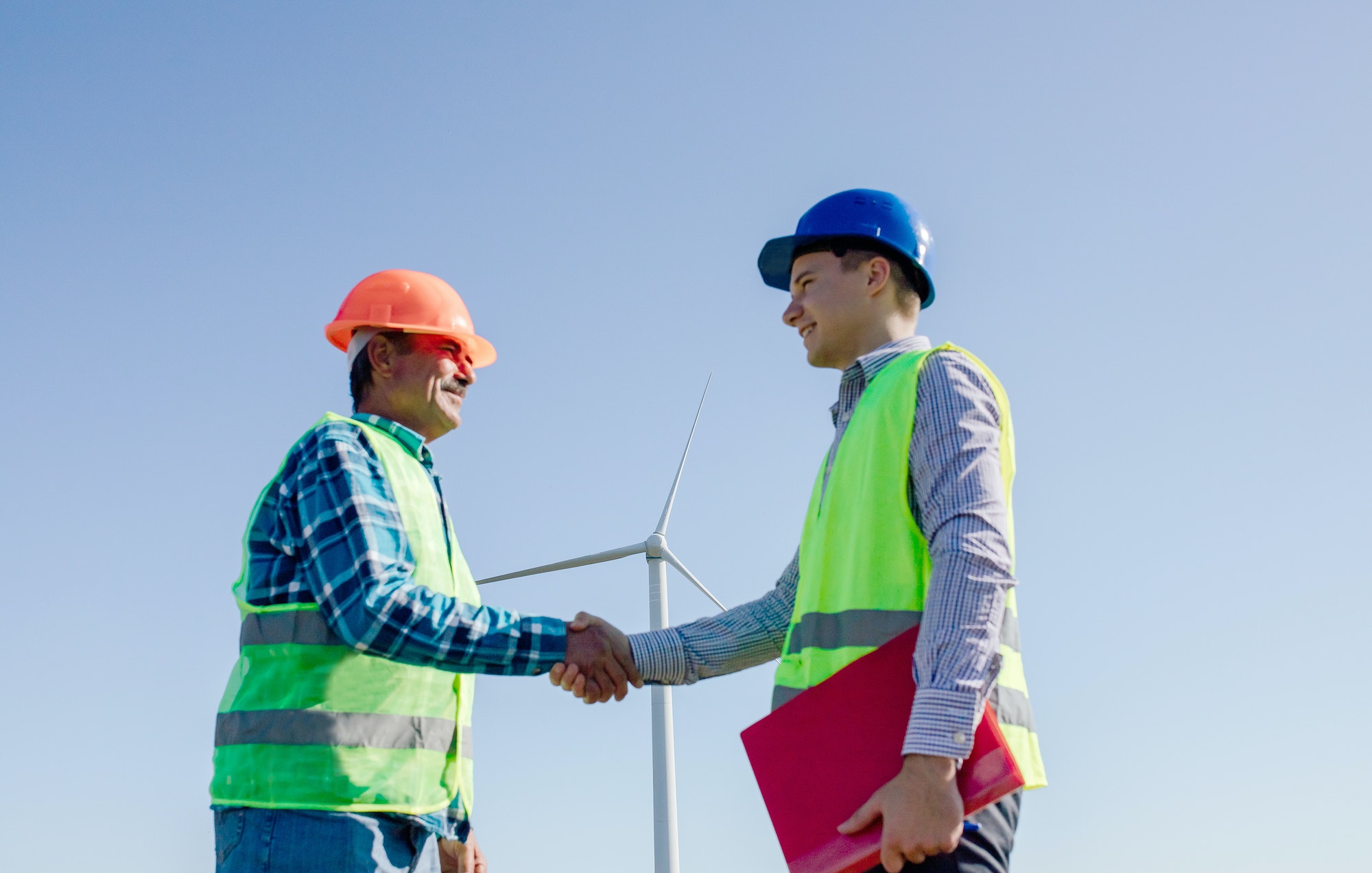 Happy engineers shaking hands near windmill